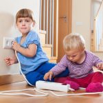 Kind bereikt naar stopcontact als voorbeeld van stekkerveiligheid risico's voor kinderen in huis